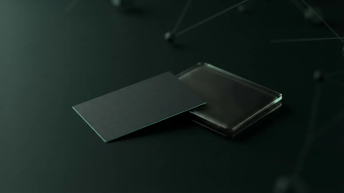 Blank charcoal card and dark glass wallet on a deep green surface